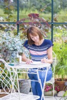 Woman sitting at table writing in a greenhouse filled with plants