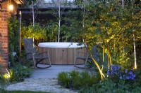 Illuminated hidden garden with jacuzzi and rocking chairs in the evening.