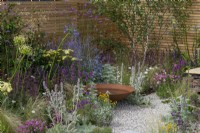 A rusted iron water bowl is edged in nectar rich perennials such as sea hollies, verbena, perovskia, salvia, sea pinks, betony and lamb's ear.