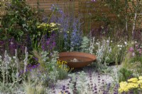 A rusted iron water bowl is edged in nectar rich perennials such as sea hollies, verbena, perovskia, salvia, sea pinks, betony and lamb's ear.