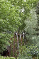 Medite Smartply Building The Future. An edge of the forest garden with a feature waterfall made from Medite Smartply, a sustainable and innovative wood-based panel product. Foliage dominates. Designer: Sarah Eberle. RHS Chelsea Flower Show 2022. Gold Medal.