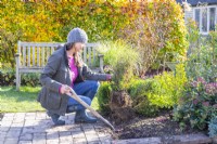 Woman using fork to dig up box hedge