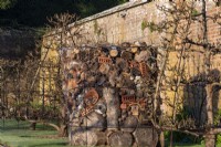 A bug hotel in between trained fruit trees.  It is built with logs, old terra cotta pots, air bricks, straw and fur cones, which are surrounded by wire netting.