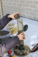 Child filling bird feeder with sunflower seeds on snowy day in winter
