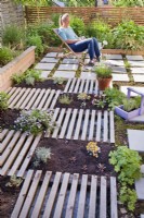 Woman relaxing on roof patio. Newly planted drought bed with herbs and succulents is separated by slats, which are decorative and at the same time serve as a path.