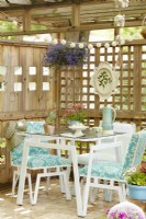 Vintage painted table and chairs on patio under a wooden pergola surrounded by trellis.
