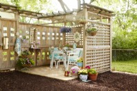 Trellised and paved patio with vintage table and chairs under a wooden pergola surrounded by trellis.