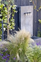 Stipa tenuissima in border with contemporary water feature in background
