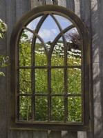 Reflections of garden in gothic mirror hanging on garden fence