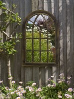Reflections of garden in gothic mirror hanging on garden fence