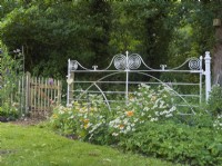 White painted wrought iron gate feature in woodland garden