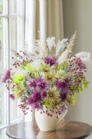 Chrysanthemum 'Tula' mixture,  seed heads of miscanthus and sprays of rose hips November. Cut flower arrangement in a cream ceramic jug.