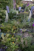 Deep cottage style garden borders studded with Granite standing stones and Galvanised steel fern by Cornish artisan 'Steeling nature'