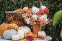 Autumn table decoration with selection of squashes arranged with bouquet of orange and white Dahlias and Chrysanthemums in orange pottery vase 