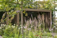 Veronicastrum 'Lavendelterm' mixed with grasses under Parrotia persica trees with metal pergola behind - Macmillan Legacy Garden: Gift the Future - RHS Hampton Court Flower Festival 2022