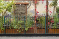 Corten steel containers with late summer perennials growing through railings, with old Indian door and wall mural - Arcadia, RHS Chelsea Flower Show 2021