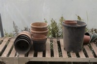 A variety of different empty pots on a wooden slatted becnh in a polytunnel. September