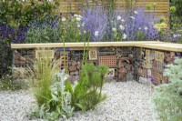 Bug or insect hotel inside gabion bench with wooden  top among  drought tolerant plants to attract pollinators, such as Salvia, Achillea, Echinops and  Perovskia - Turfed Out Garden, RHS Hampton Court Palace Garden Festival 2022
