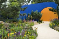 Colourful planting along curved path leading to' circular opening  - Over The Wall Garden, supported by Takeda. RHS Hampton Court Palace Garden Festival 2022