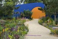 Colourful planting along curved path leading to a raising sun structure  - Over The Wall Garden supported by Takeda. RHS Hampton Court Palace Garden Festival 2022. 