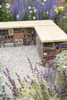 Bug or insect hotel inside gabion bench with wooden top among drought-tolerant planting including Perovskia and Salvia in gravel - Turfed Out Garden, RHS Hampton Court Palace Garden Festival 2022. July. 