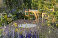 Sitting area with wooden table and chairs and planting of  Allium sphaerocephalon, Achillea 'Coronation Gold' , Agastache and Perovskia in Joy club garden - RHS Hampton Court Palace Garden Festival 2022