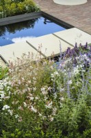 Stepping-stone bridge over rill water feature with delicate cloud planting of  Perovskia and Gaura  in The Joy Club Garden at RHS Hampton Court Palace Garden Festival 2022