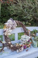 Rustic willow wreath decorated with dried hydrangeas and roses on wooden garden bench