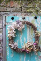 Willow wreath decorated with dried hydrangeas and roses hanging against old painted door