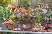 Autumn table arrangements including woven box and glass stand with apples and terracotta decorated with rose hip wreath and filled with hydrangea, asters, guelder rose and euonymus.