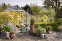 Greenhouse framed by pots and galvanised watering cans in a country garden in April