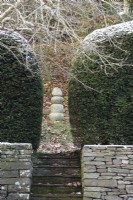 Focal point of stacked stones framed by yew hedges in a garden in December.