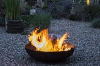 A blazing fire pit on gravel in a contemporary courtyard garden.