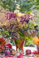 Bouquet containing hydrangea flowers, privet twigs with berries and glory tree in glass vase.