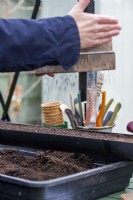 Woman using a compost sieve to evenly spread compost over the seeds