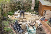 An overview of the makeover of a small London garden in progress including  a worker laying York Stone slabs for a terrace at the rear of the garden.