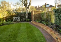 An 'After Photo' of a London garden after a makeover with a new low brick wall, brick path, York Stone terrace and newly laid turf.