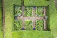View over small rectangular garden contained within mature clipped Yew hedges. Six beds of late summer herbaceous planting divided by brick paths with seats. Image taken from drone. July.