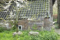 Blossom tree with root ball in front of farmhouse with wooden sign near tree nursery Floris bomen.