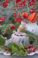 Winter arrangement with frozen cake, spruce branches and bouquet of Chinese lanterns and guelder rose twigs with berries.