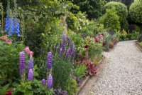 Summer mixed border in the Kitchen Garden at Morton Hall with lupins, heuchera, roses and delphiniums and arch in brick wall behind..
