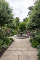 View down the path in the South Garden at Morton Hall Gardens past borders with roses and herbaceous towards the pool and fountain.