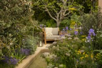 Iris pallida var. pallida, Foeniculum vulgare, Artemisia 'Powis Castle',  and Pimpinella major 'Rosea' around a secluded seating area in the Hamptons Mediterranean Garden, a sanctuary garden designed by Filippos Dester at the RHS Chelsea Flower Show 2023