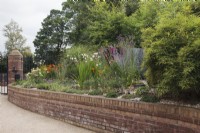 Large raised bed with curved retaining brick wall in front garden with Gladiolus, Echinaceas, Heleniums, Crocosmias and bamboo - August