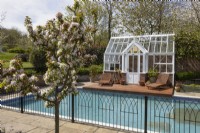 Four Seasons Garden, representing a walled town house garden with greenhouse & swimming poo. Malus, Golden Hornet, crab apple trees in blossom in the foreground. Trago Mills show gardens, Devon, UK. May. Spring
