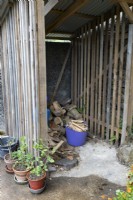 A log store with timber slatted sides and a variety of pots to the side.