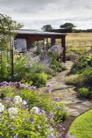 White and purple themed perennial border, featuring phlox and campanula, by crazy paving path to conservatory