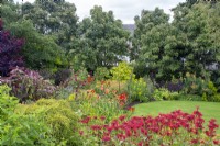 Perennial border by circular lawn featuring Monarda 'Gardenview Scarlet', hemerocallis, euphorbia etc in North House Garden