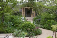 A winding path leads between borders planted with a range of trees, shrubs and perennials to foster biodiversity, passing a seating area before arriving at a timber summerhouse.