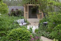 A summerhouse overlooks a seating area immersed amongst borders planted with a range of trees, shrubs and perennials to foster biodiversity.
